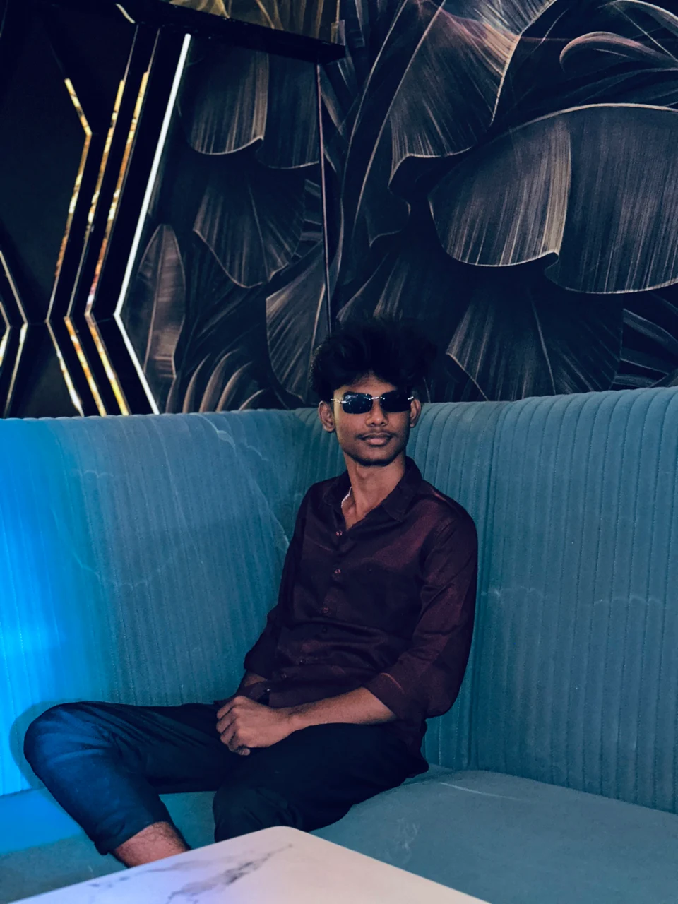 Vikash Saravanan seated on a blue sofa wearing sunglasses